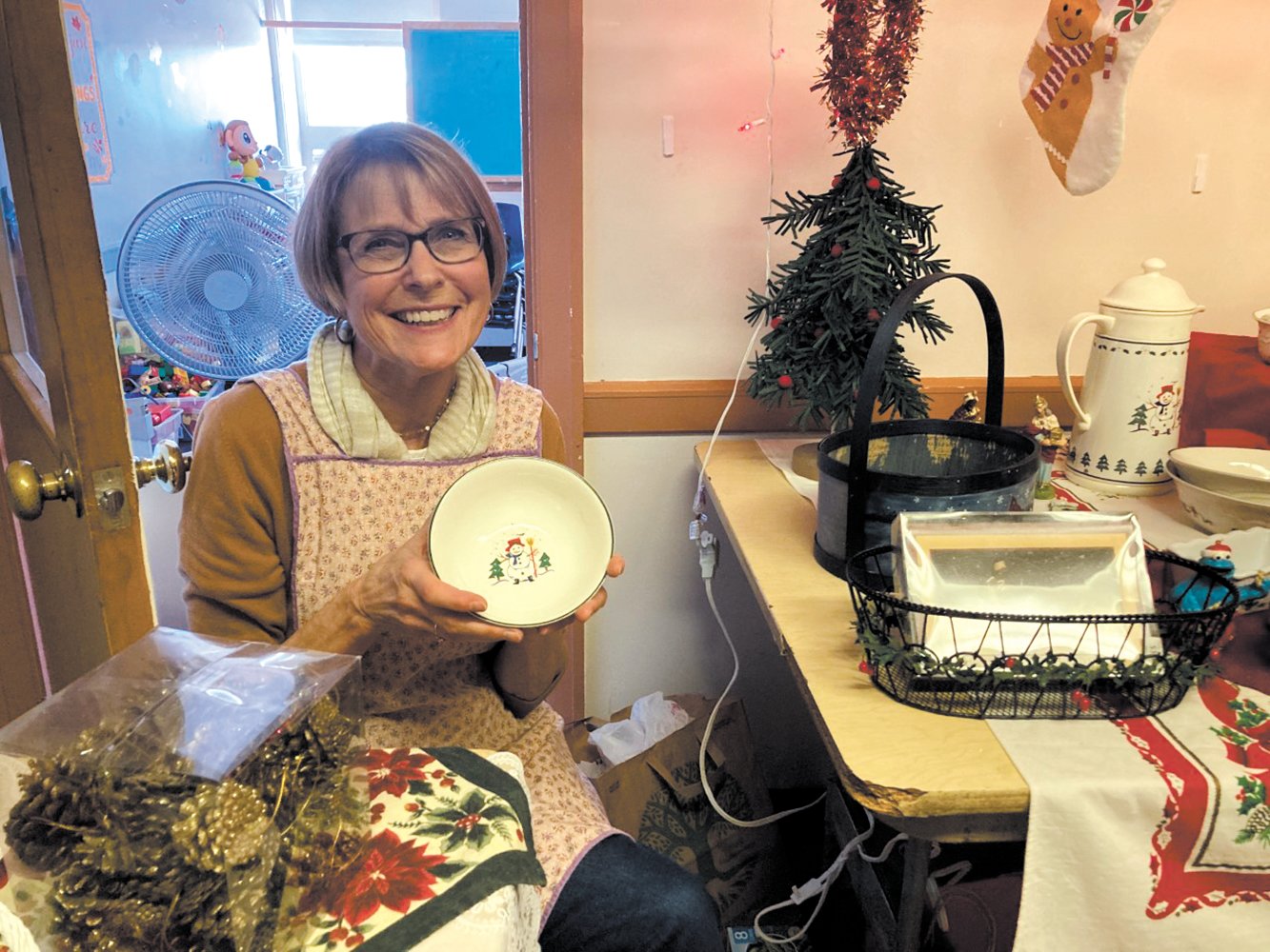 CHRISTMAS TREASURES: Barbara Spencer, the minister’s wife, assisted shoppers in finding just the right item to take home. Among some of the kitchenware were holiday dishes with snowmen.